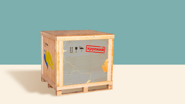 Wooden shipping crate against a light blue and cream background. The crate has a map with Cyrillic text, fragile symbols, and a colorful bird graphic on the side.