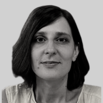 A black and white portrait of a person with shoulder-length hair, wearing a sleeveless top, against a plain background.