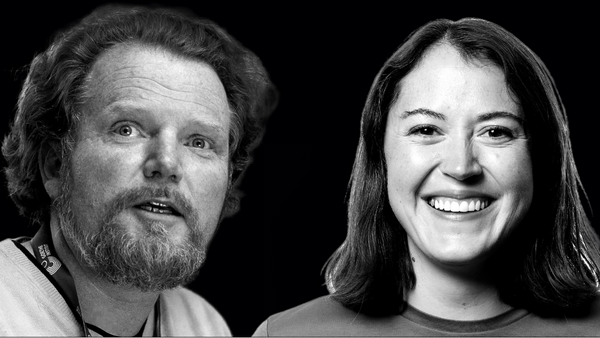 A black and white photo of a man and a woman. The man has curly hair, a beard, and is wearing a lanyard. The woman has shoulder-length hair and is smiling. Both are set against a dark background.