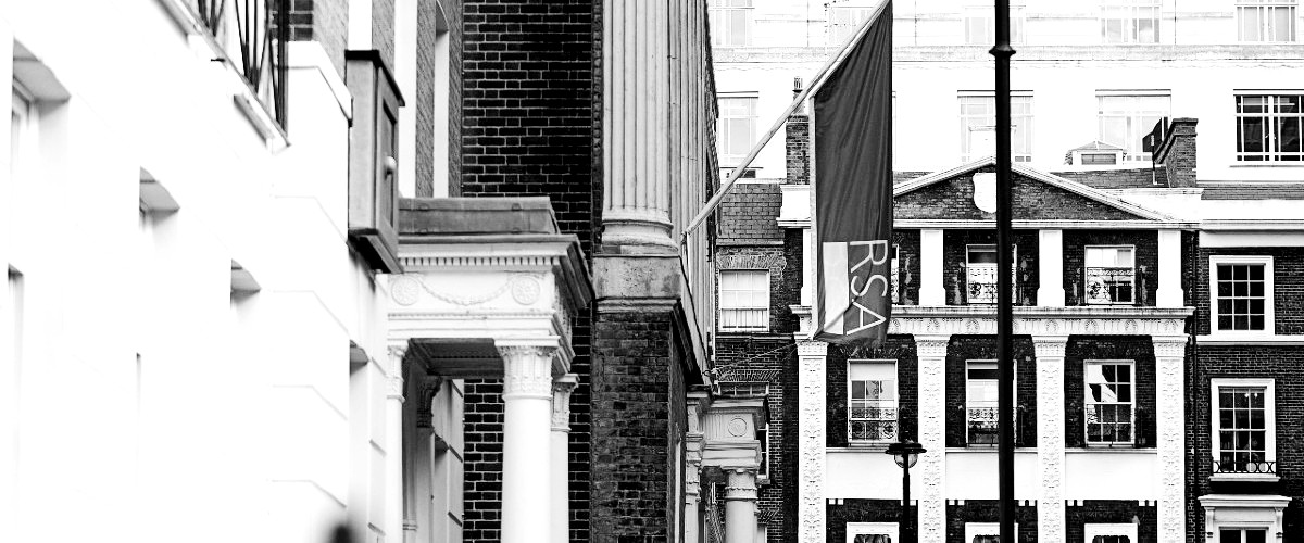 Black and white photo of a street with classic architecture. Columns and brickwork are visible. An RSA banner hangs from a pole in front of a building. Multiple windows and some building details are in the background.