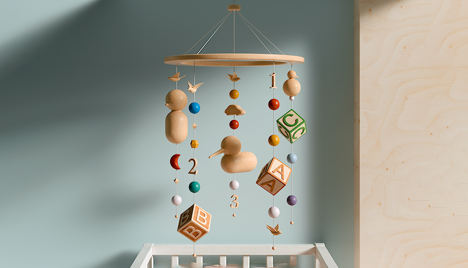 A wooden baby mobile hangs above a crib with colorful elements including blocks with letters and numbers, a duck, a cloud, and various beads in red, blue, yellow, and green. The wall is a soft teal color.