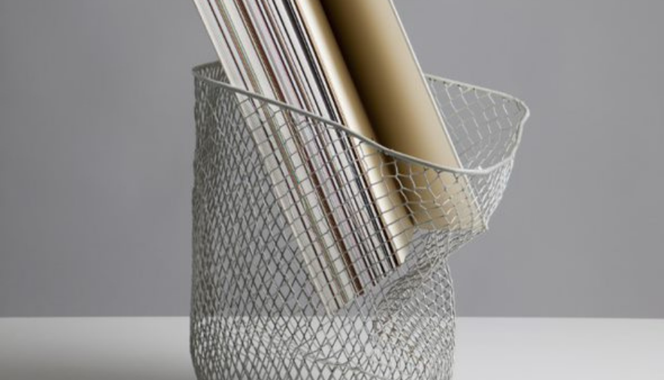 A wire mesh trash can holds several rolled-up posters. The can is placed on a white surface against a gray background.