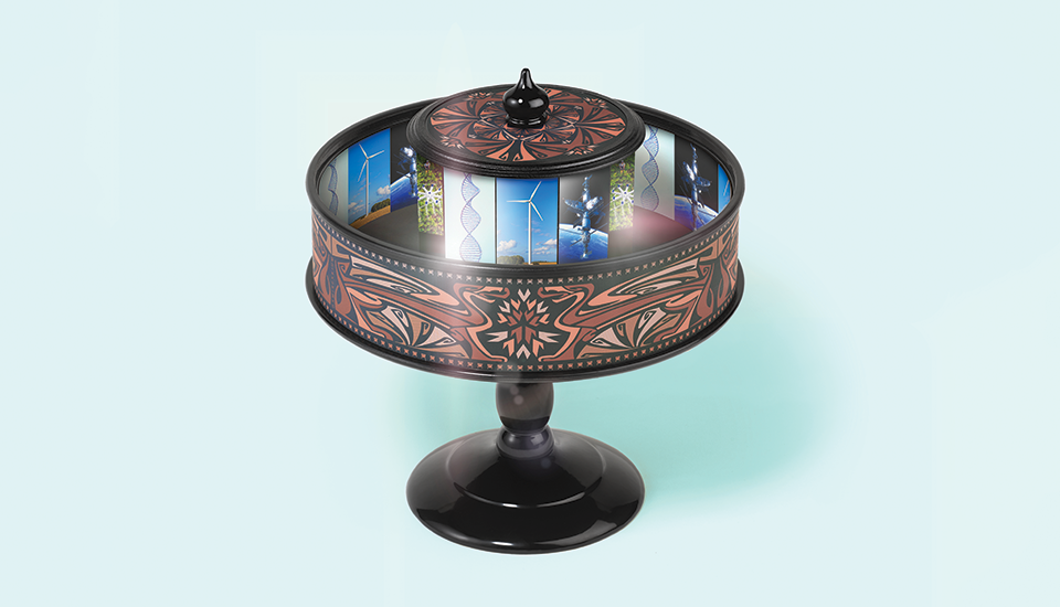 A black praxinoscope with ornate red patterns stands on a light blue background. Inside, mirrored panels reflect a series of colorful images, creating an illusion of motion. The device has a decorative lid on top.
