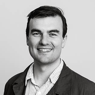 Smiling Toby Murray with short hair wearing a shirt and jacket. The image is black and white.