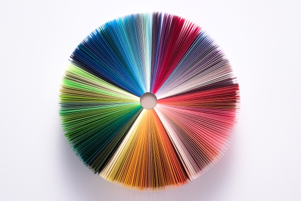 Circular array of colored paper sheets fanned outward, creating a vibrant spectrum. Each section transitions smoothly through various hues, forming a colorful wheel against a plain white background.