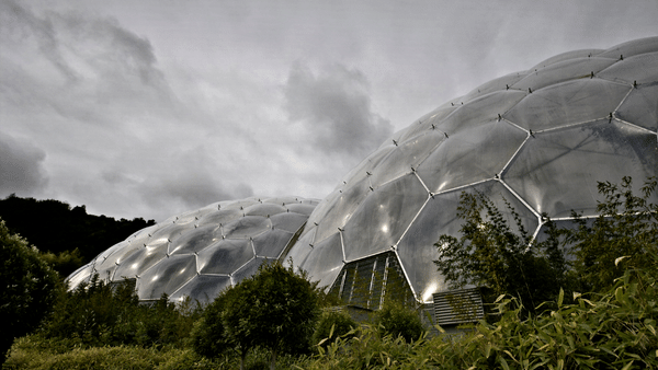 A view of large geodesic domes with transparent panels, surrounded by green foliage. The sky is overcast with grey clouds, creating a dramatic atmosphere.