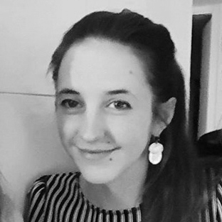 Black and white photo of a person with long hair pulled back, wearing a striped top and large earrings. They are smiling slightly and looking towards the camera.
