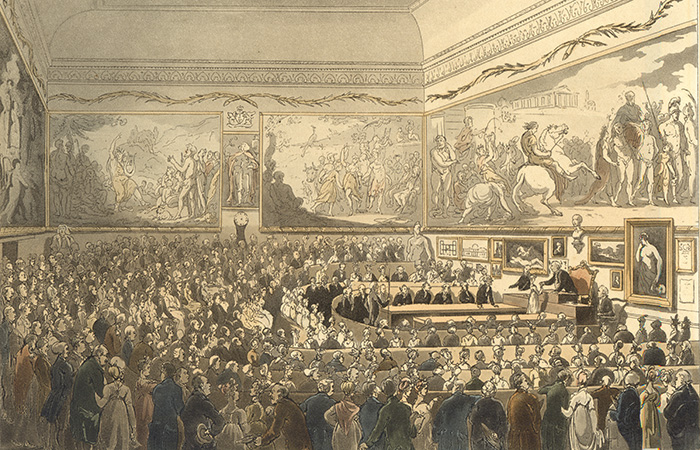 A historic illustration of a crowded assembly hall with numerous people gathered around a central table. The walls are adorned with large, detailed murals depicting various scenes and figures. The setting appears formal and ceremonial.