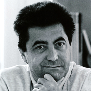 Black and white photo of a middle-aged person with short, dark hair, resting their chin on their hand, wearing a light-colored shirt. They have a thoughtful expression, with a blurred background.