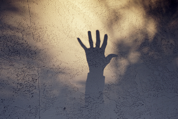 Shadow of a hand with fingers spread against a textured wall, surrounded by soft, dappled light and shadow patterns creating an artistic effect.