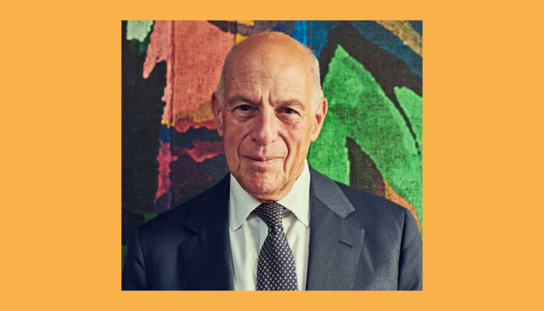 Man in a suit and tie stands against a colorful abstract background with shades of pink, blue, green, and black, set within an orange frame.