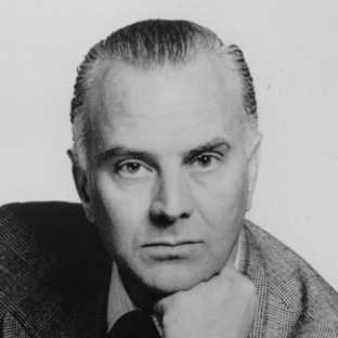 Black and white portrait of a person with short hair, wearing a suit jacket. They rest their chin on their hand and look directly at the camera.