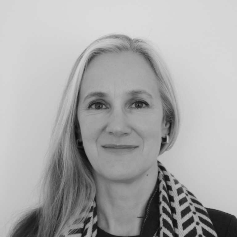 Black and white portrait of a person with long, straight hair wearing a patterned scarf and earrings, smiling softly against a plain background.
