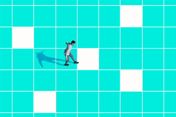 Person walking on a large, blue and white checkerboard pattern. Their shadow is elongated on the bright surface, emphasizing the geometric design.