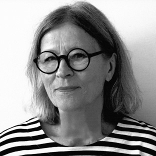 A black and white portrait of an older person with shoulder-length hair, wearing round glasses and a striped shirt, looking slightly to the side with a neutral expression.