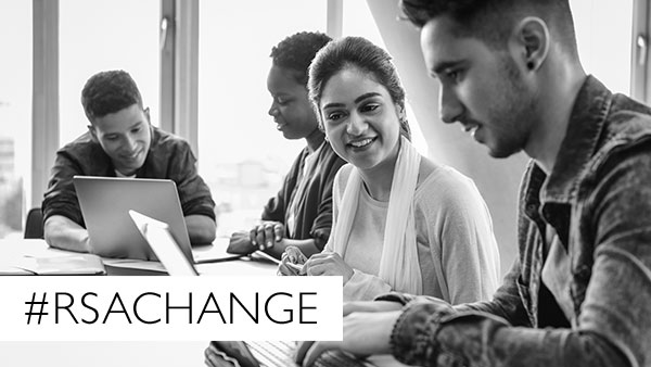 A diverse group of four people are sitting at a table, engaged in discussion and working on laptops. A hashtag "#RSACHANGE" is overlaid on the image. The setting appears to be a bright, modern office or classroom.