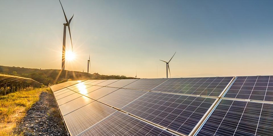 Solar panels in the foreground capture sunlight on a clear day, while wind turbines stand tall in the background on a grassy hill. The sun is near the horizon, casting warm light across the landscape, highlighting the renewable energy theme.