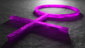 A 3D-rendered purple Venus symbol lies on a textured gray surface. The symbol, representing femininity, is depicted with a glowing effect, casting soft shadows and creating a visually striking contrast with the background.