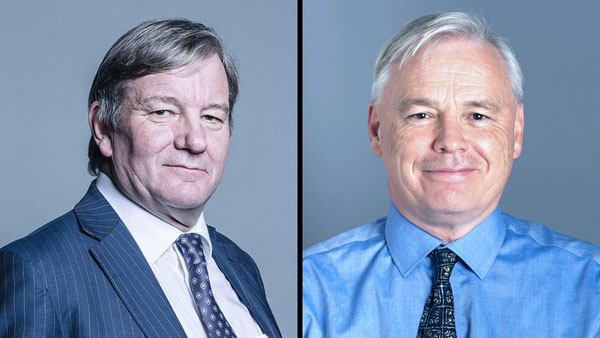 Two men are pictured side by side on a split screen. The man on the left wears a dark pinstripe suit and tie, while the man on the right wears a light blue shirt and patterned tie. Both men have light-colored hair and face the camera against a neutral background.