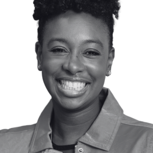 A person smiling at the camera, wearing a jacket. The black and white photo captures their cheerful expression and curly hair as we join them to celebrate the opening of the UK Pavilion at Expo 2025 Osaka, highlighting leading innovators from both the UK and Japan.
