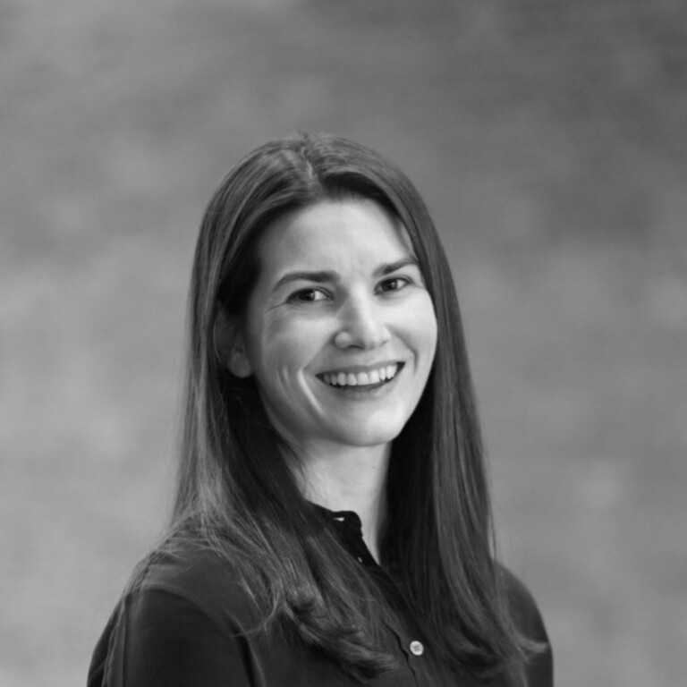 Black and white portrait of a woman with long straight hair, smiling, wearing a dark buttoned shirt. The background is plain and softly blurred. Join us to celebrate the opening of the UK Pavilion at Expo 2025 Osaka.
