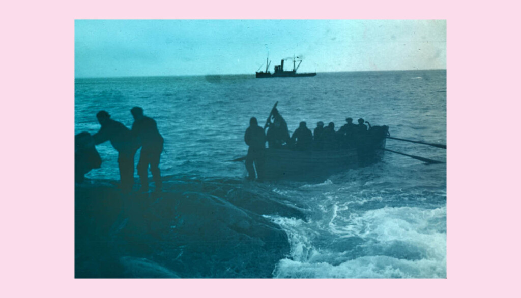 A vintage photograph showing people in a rowboat approaching a rocky shore. Some are disembarking, assisted by individuals on the rocks. A ship is visible on the horizon. The scene has a blue tint.