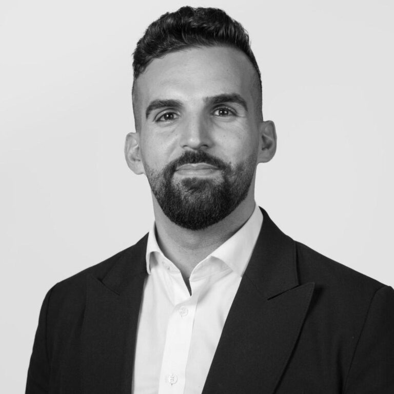 A man with short dark hair and a beard, wearing a dark suit jacket over a white shirt, poses in front of a plain light background—perfect for promoting events on sustainability or the UN Sustainable Development Goals.
