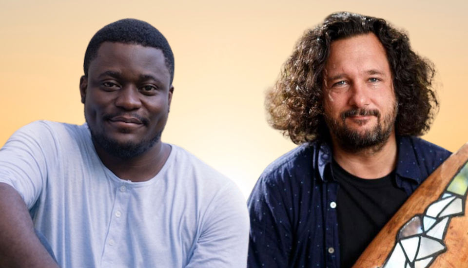 Two men are posing against a gradient background. The man on the left is wearing a light blue shirt and is smiling softly. The man on the right has curly hair, is wearing a dark shirt, and is holding a decorated wooden object.