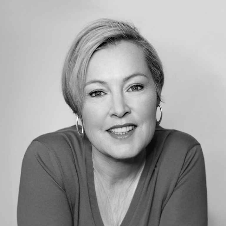 A woman with short, light hair and hoop earrings smiles at the camera. She is wearing a V-neck top and is posed against a plain, light background at a Ukraine event. The image is in black and white.