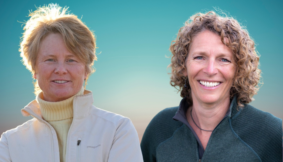 Two smiling women against a gradient sky background. One has short hair and wears a light turtleneck and jacket. The other has curly hair and wears a darker zip-up jacket. Their faces are lit with soft lighting.