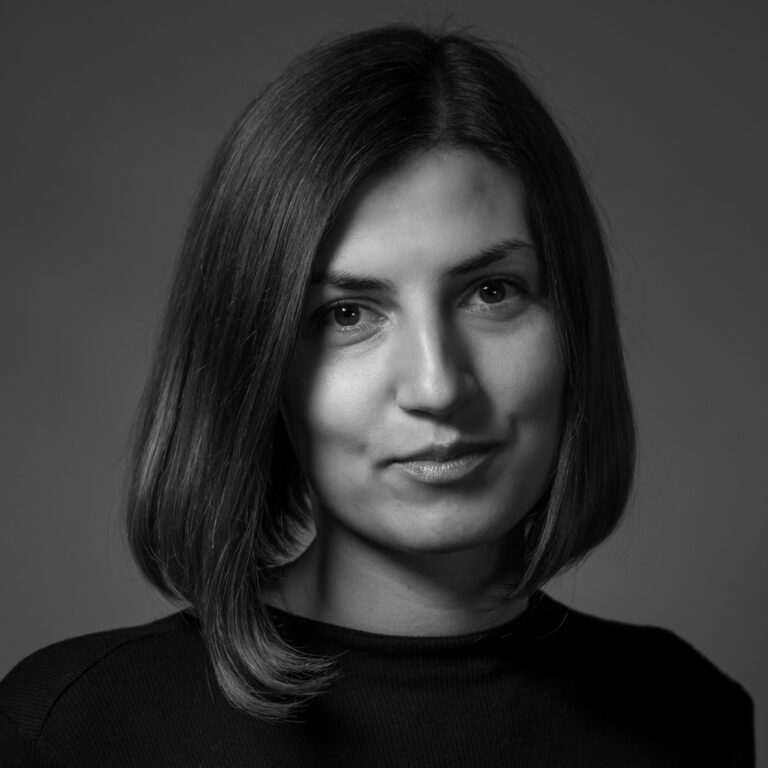 Black and white portrait of a woman with straight, shoulder-length hair, wearing a dark top, looking at the camera with a neutral expression, captured in the style of portraits showcased at Expo 2025, against a plain background.