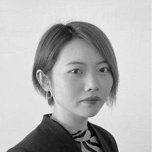Black-and-white portrait of a person with short, straight hair, wearing a dark blazer and patterned top, looking confidently at the camera against a plain background—capturing the strength and spirit that connect them to their community.