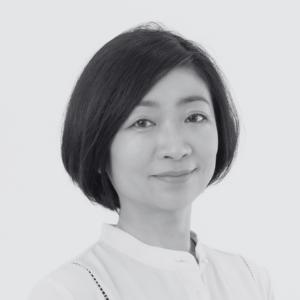 A woman with short, straight black hair, wearing a white collared shirt, looks at the camera with a slight smile against a plain, light background.