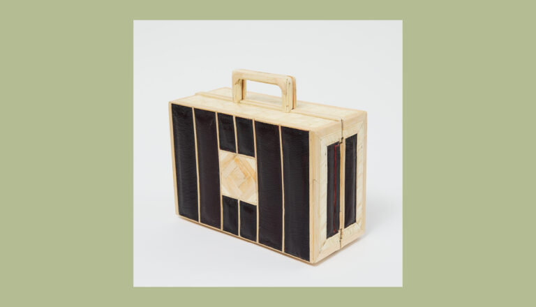 A rectangular, briefcase-shaped object with a wooden frame and handle, featuring vertical black panels and a central square pattern, displayed on a plain light background with a wide olive border.