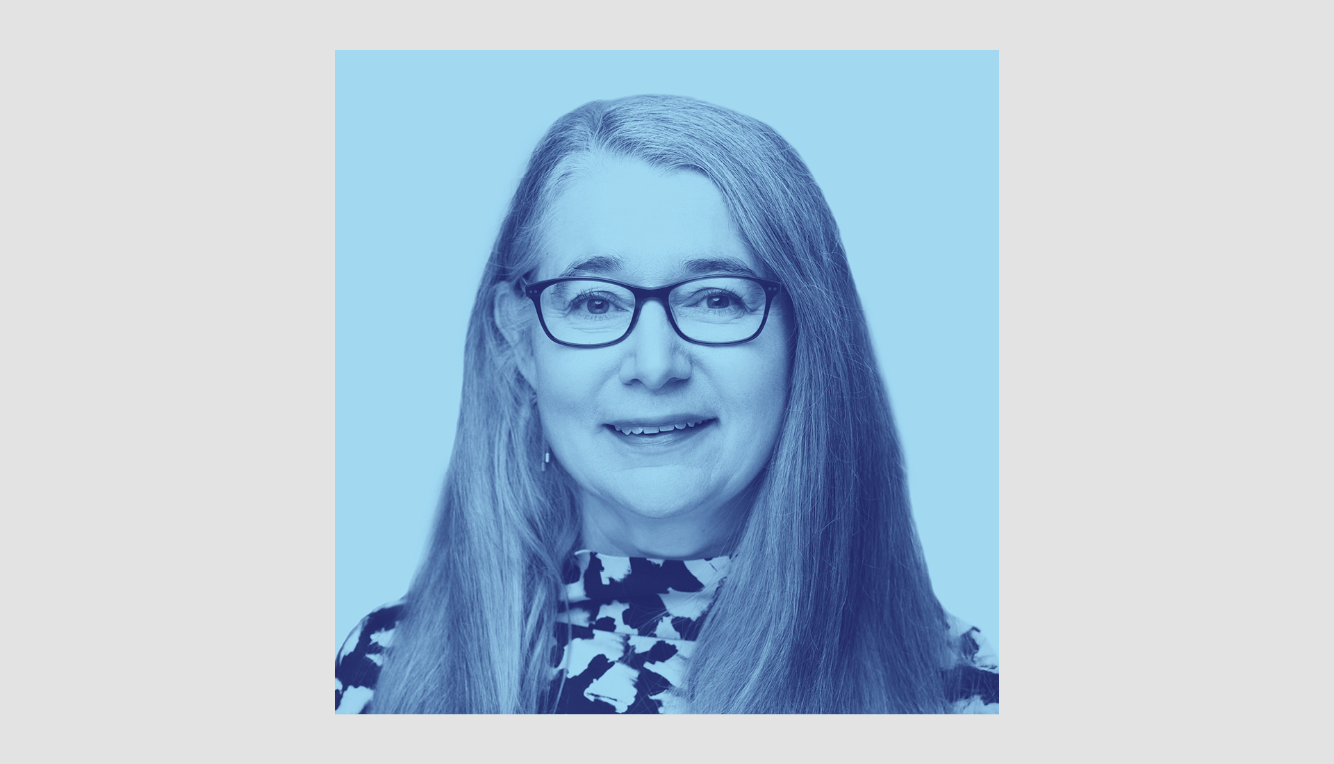 An image of Sophie Hussey with long straight hair and glasses smiles at the camera. She is wearing a patterned top and the image has a blue color filter.