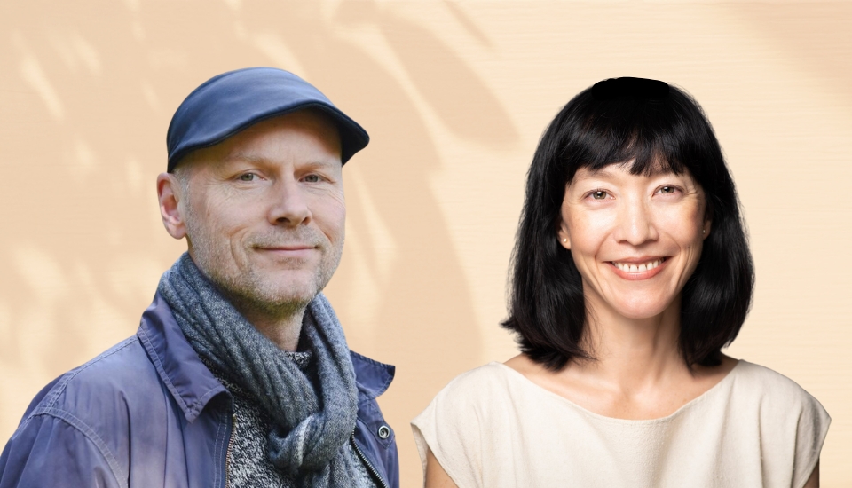A man wearing a blue cap and scarf stands next to a woman with medium-length black hair and a beige top. Both are smiling, with a soft beige background behind them.