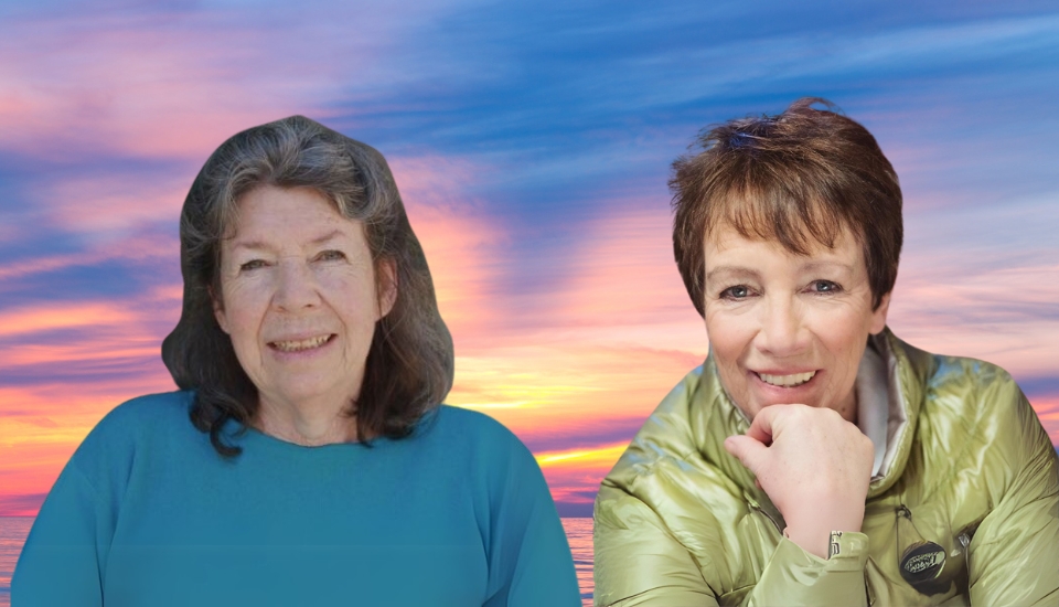 Two women smiling in front of a vibrant sunset sky with soft clouds. One woman has long, wavy gray hair and wears a blue top; the other has short brown hair, a green jacket, and rests her chin on her hand.
