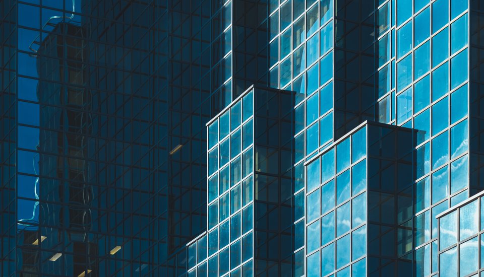 Close-up of a modern glass building with multiple geometric sections, reflecting the sky and clouds on its shiny blue windows—an inspiring sight often featured at leading architecture events in London.