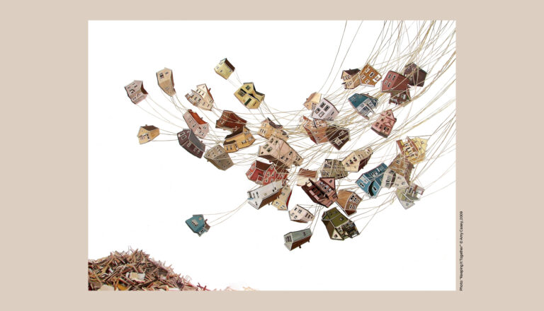 Small, colorful paper houses are suspended in midair by strings, appearing to float upward from a pile of shredded paper, symbolizing the future of education against a clean white background.
