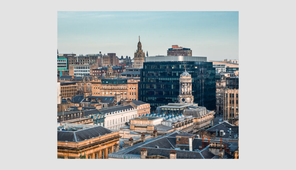 A cityscape featuring a mix of historic and modern buildings under a clear blue sky, with a prominent black glass building and a domed structure among older, ornate rooftops.
