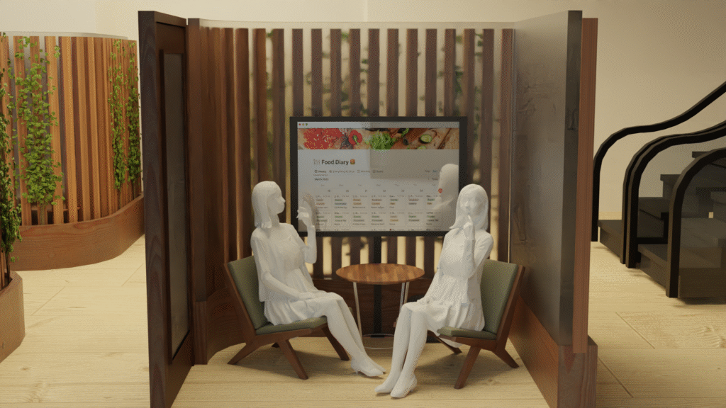 Two white mannequins sit in chairs around a small table in a modern wooden booth, looking at a large screen displaying a food delivery website. Green plants and part of a staircase are visible in the background.