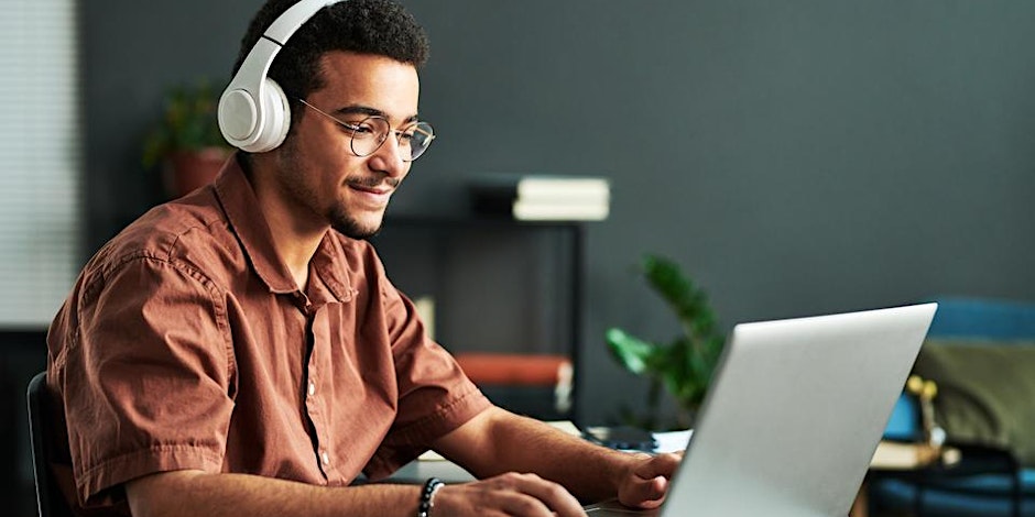 A young man wearing headphones and glasses sits at a desk, smiling while using a laptop to join an RSA webinar in a modern, softly lit room with books and plants in the background.