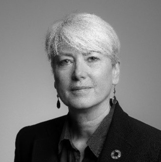 Black and white portrait of a person with short, light-colored hair, wearing a blazer, collared shirt, and drop earrings—capturing the spirit of inclusive growth in the East Midlands as they look directly at the camera with a neutral expression.