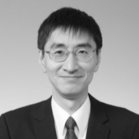 Black and white portrait of a man wearing glasses, a suit, and a tie, smiling softly at the camera against a plain background—captured for the Edward Boyle Lecture.