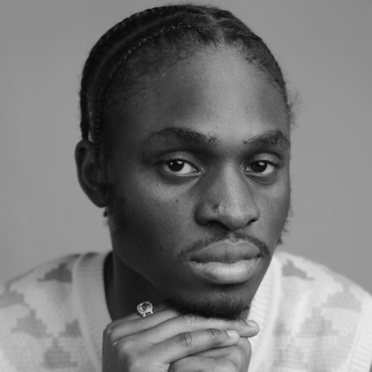 Black and white portrait of a person with braided hair, wearing a patterned sweater and a ring, resting their chin thoughtfully on their hand while looking into the camera at a New Black Film Collective film screening.