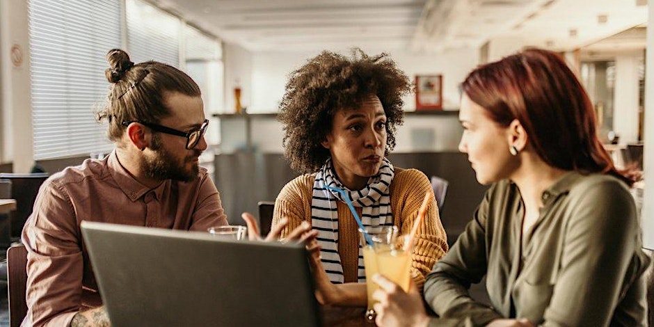Three people sit at a table in an office, engaged in a serious discussion. A laptop is open in front of them, and one person holds a glass of juice. Sunlight streams through the windows in the background.