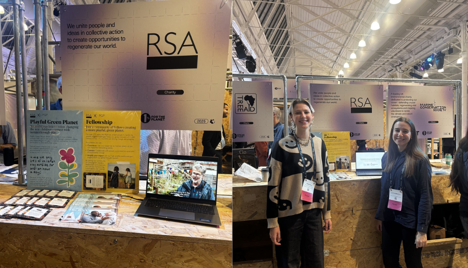 A booth display for RSA at an indoor event. The booth features informational posters, a laptop, promotional materials, and two women smiling and standing in front of the display. Other booths are visible in the background.