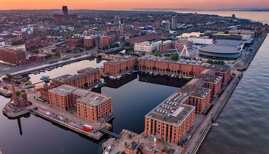 Aerial view of Liverpool’s Royal Albert Dock at sunset, with brick warehouses, a Ferris wheel, and modern buildings—perfect inspiration for those seeking events in Manchester or planning their next Manchester event by the waterfront.